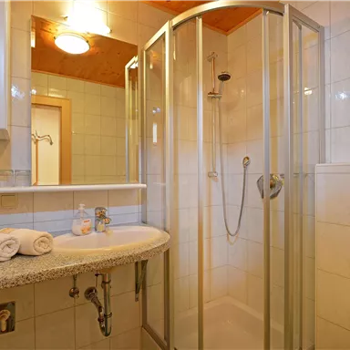 A modern bathroom with a shower cabin and a sink. Fresh towels are ready, and the walls are brightly tiled.