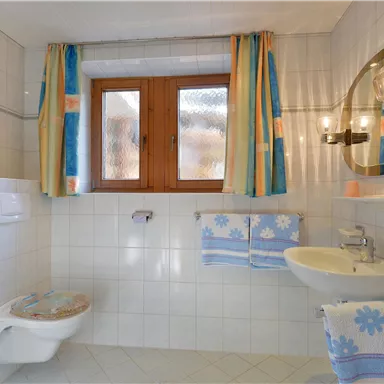 A clean bathroom with white tiles and colorful curtains. There is a sink, a toilet, and a large mirror.