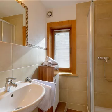 A modern bathroom with a shower and a sink. Bright tiles and a window create an inviting atmosphere.