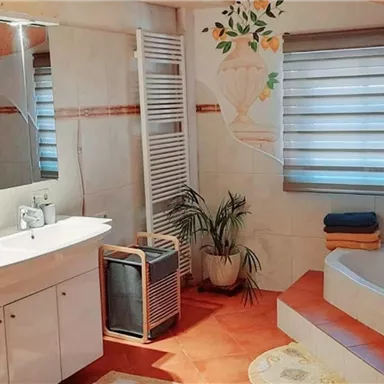 Ein modernes Badezimmer mit einer Badewanne und einem großen Spiegel. Die Wände sind hell, und es gibt Pflanzen sowie Handtücher für eine einladende Atmosphäre.