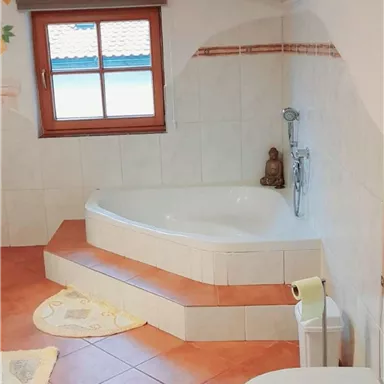 Ein modernes Badezimmer mit einer runden Badewanne und einer Toilette. Große Fenster sorgen für viel natürliches Licht.
