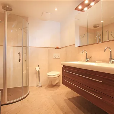 A modern bathroom with a shower, a large sink, and a toilet. The bright tiles and wood design create an inviting atmosphere.