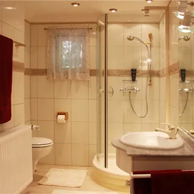 A modern bathroom with a shower and a sink. The walls are brightly tiled and there are towels in red colors.