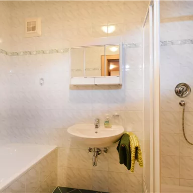 A modern bathroom with a bathtub, shower, and sink. The walls are brightly tiled and the room feels clean and welcoming.