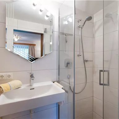 Ein modernes Badezimmer mit einer Dusche aus Glas und einem Waschbecken. Die Wände sind in neutralen Farben gehalten und es gibt weiche Handtücher.