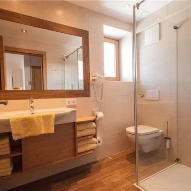 A modern bathroom with a shower, a sink, and a large mirror. The wooden details and bright colors create an inviting atmosphere.