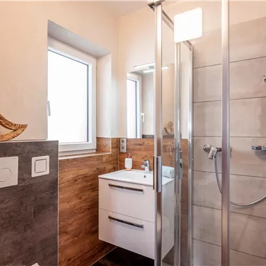 A modern bathroom with a shower and a sink. The walls are in neutral colors, and a large window provides natural light.