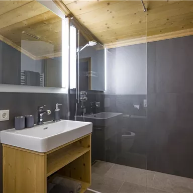 Ein modernes Badezimmer mit einem Holzwaschtisch und einer großen Dusche. Die Wände sind in neutralen Tönen gehalten, und es gibt viel natürliches Licht.