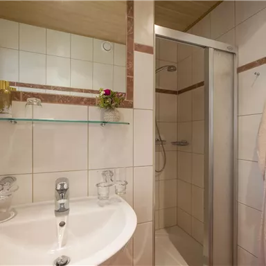 Ein modernes Badezimmer mit einer Dusche und einem Waschbecken. Die Wände sind gefliest und eine Handtuchstange ist sichtbar.