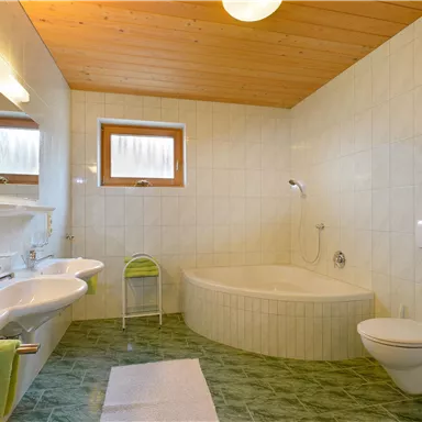A modern bathroom with a bathtub and a toilet. Bright tiles and wooden ceilings create a friendly atmosphere.