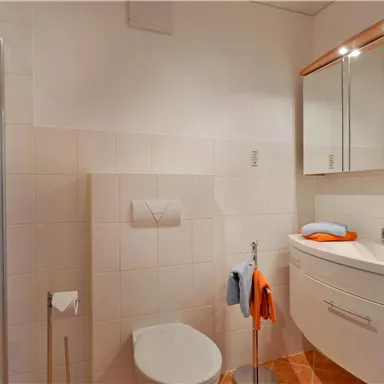 A modern bathroom with a shower and a sink. It is bright and well-designed, with white tiles and warm wood tones.