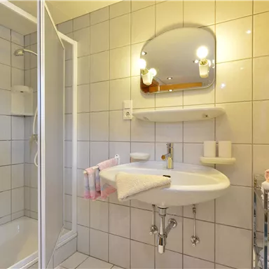 A modern bathroom with a shower and a sink. Towels are neatly arranged on a shelf.
