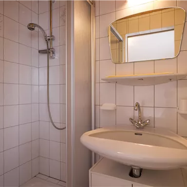 Ein modernes Badezimmer mit einer Dusche und einem Waschbecken. Die Wände sind gefliest, und ein Spiegel hängt über dem Waschbecken.