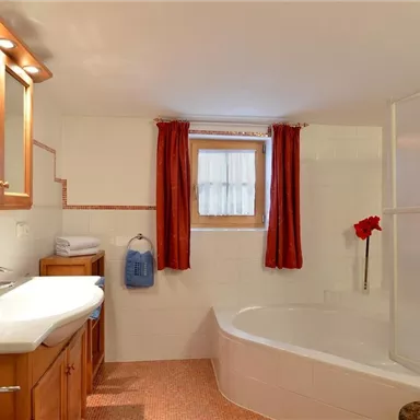A modern bathroom with a bathtub and a shower cabin. The white tiles and red curtains create a bright, inviting atmosphere.