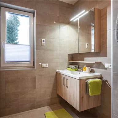 Ein modernes Badezimmer mit einer Holzwaschtisch und einem großen Spiegel. Hellgraue Fliesen und grüne Handtücher sorgen für eine frische Atmosphäre.