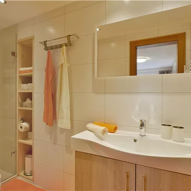 Ein modernes Badezimmer mit einer Dusche und einem Waschbecken. Es gibt Holzregale und nützliche Accessoires in neutralen Farben.