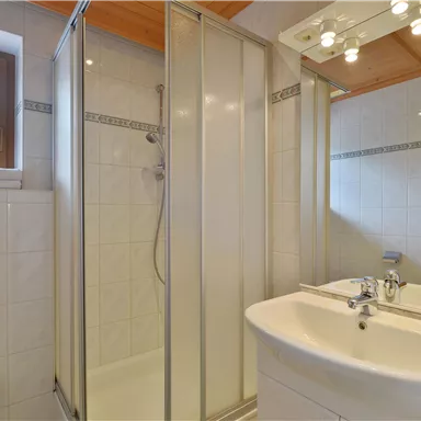 A modern bathroom with a shower cubicle and a sink. The walls are designed with white tiles and there is plenty of natural light.
