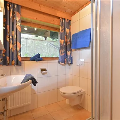 Ein modernes Badezimmer mit einer Dusche und einem Waschbecken. Die Fenster lassen viel Licht herein und die farbenfrohen Vorhänge verleihen dem Raum ein frisches Ambiente.