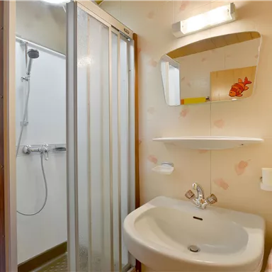 A small bathroom with a shower and sink. The walls are bright and adorned with subtle decoration.