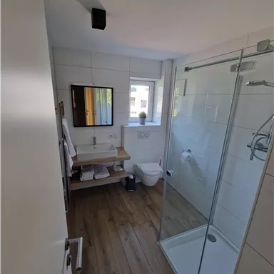 Ein modernes Badezimmer mit einer Dusche und einem WC. Es gibt einen Spiegel und eine kleine Ablage mit Handtüchern.