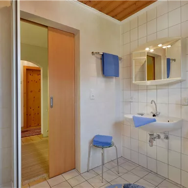 A modern bathroom with white tiles and blue towels. The bathroom features a shower, a sink, and a large mirror.