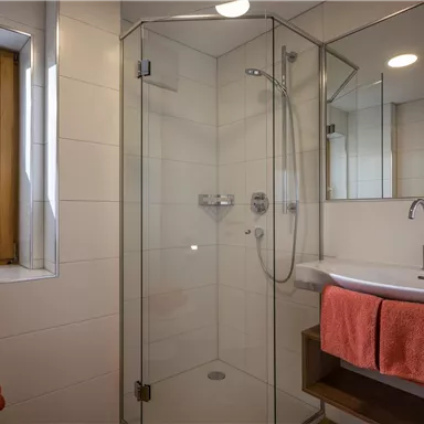 A modern bathroom with a glass shower and a vanity. The towels are in bright orange.