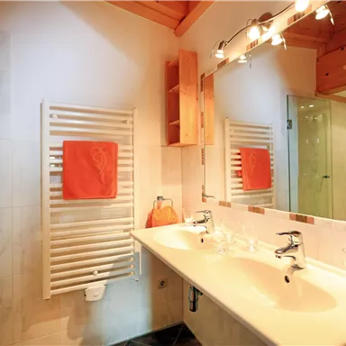A modern bathroom with a double sink and a large mirror. White towels hang on the wall and there is a shower area with glass partition.