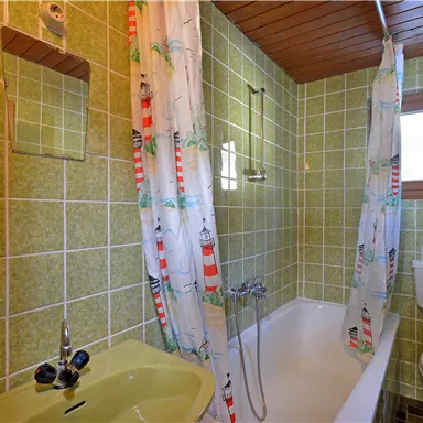A simple bathroom with green tiles. There is a bathtub, a toilet, and a small mirror.
