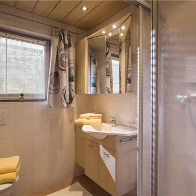 A modern bathroom with a white shower, mirror, and wooden ceiling. Yellow towels are placed on the sink.