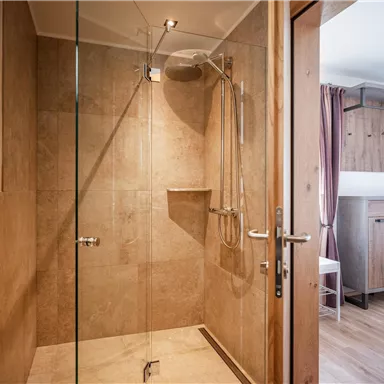 Ein modernes Badezimmer mit einer begehbaren Dusche aus Glas und hellem, natürlichem Holz. Die Wände sind in warmen Erdtönen gehalten.