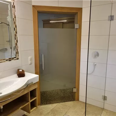 Ein modernes Badezimmer mit einer eleganten Dusche und einem Waschbecken. Die Wände sind hell gefliest und die Einrichtung ist minimalistisch.