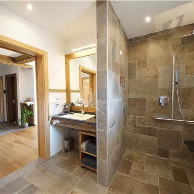 A modern bathroom with an elegant shower and stylish tiles. There is also a washing area with wooden details.