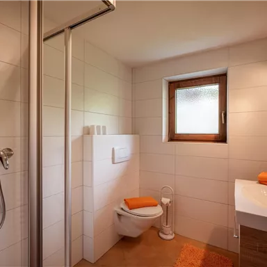 A modern bathroom with a shower, toilet, and sink. Bright tiles and orange towels create a pleasant atmosphere.
