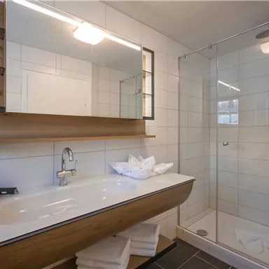 A modern bathroom with an elegant shower and a large mirror. The white tiles and wooden details create a simple, harmonious atmosphere.