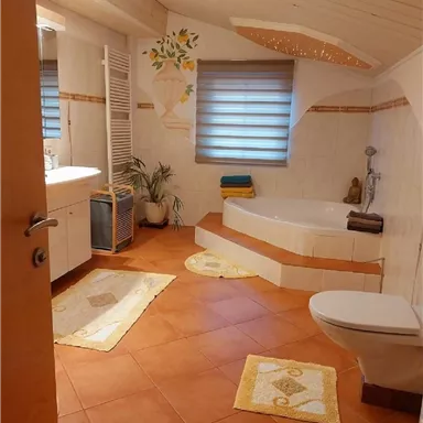 Ein modernes Badezimmer mit einer Badewanne und einem Waschbecken. Der Raum ist hell und freundlich mit dekorativen Elementen und Terrakottaboden.