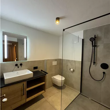 A modern bathroom with a glass shower and elegant gray tiles. The wooden sink complements the simple, stylish decor.