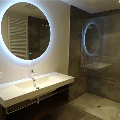 A modern bathroom with two round mirrors and a glass shower. The walls are in neutral gray tones, and the sink has a simple, elegant shape.