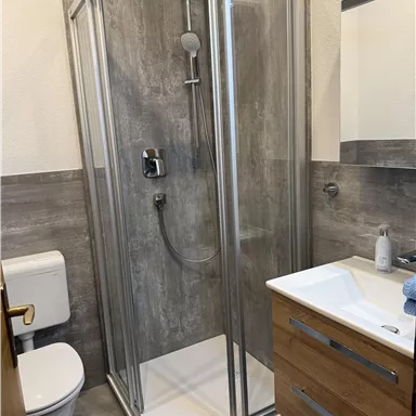 Ein modernes Badezimmer mit einer gläsernen Dusche und einem Holzwaschbecken. Die Wände sind in neutralen Farbtönen gehalten.