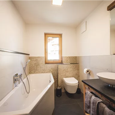Ein modernes Badezimmer mit Badewanne, Waschbecken und Toilette. Das Licht kommt durch ein Fenster und sorgt für eine helle, einladende Atmosphäre.