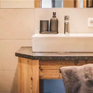 Ein modernes Waschbecken auf einem Holztisch in einem stilvollen Badezimmer. Die Wände sind hell und einfach gestaltet, mit dezenten dekorativen Elementen.