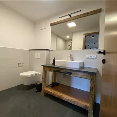 Ein modernes Badezimmer mit einer großen Holzkommode und einem schlichten Waschbecken. Die Wände sind hell, und der Boden ist dunkel gefliest.