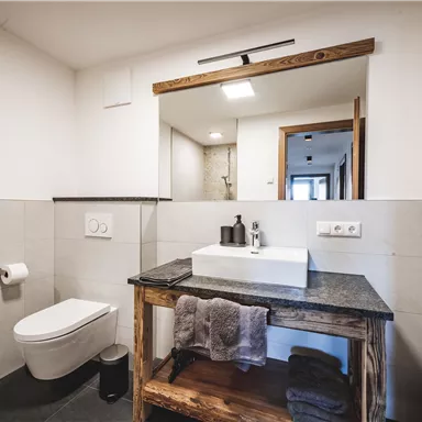 Ein modernes Badezimmer mit einem Waschbecken auf einer Holzbank und einem eleganten Toilettenbereich. Die Wände sind hell gestaltet und es gibt ausreichend Licht.