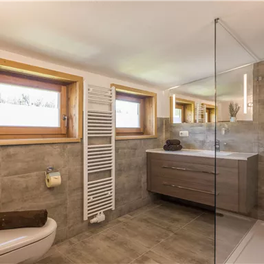 A modern bathroom with a large shower and a stylish wooden sink cabinet. The windows provide plenty of daylight and a pleasant atmosphere.