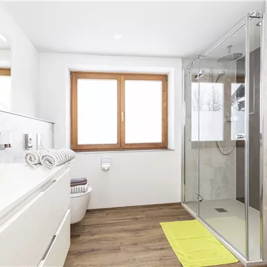 A modern bathroom with a large shower and a bright window. The furnishings are clean and well-structured, with an elegant sink and towels.