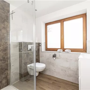 A modern bathroom with a shower, toilet, and sink. Large windows provide bright light and a pleasant atmosphere.