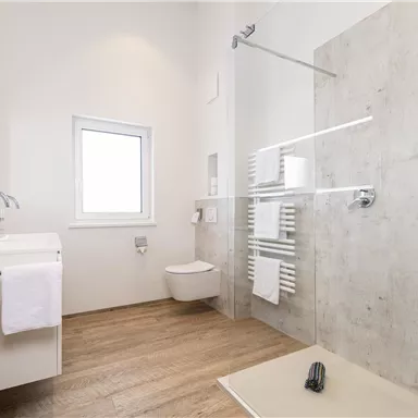 A modern bathroom with a sink, a shower, and a window. The floor is made of wood and there are fresh towels available.