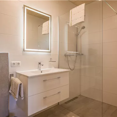 A modern bathroom with a shower and a large mirror. The walls are brightly tiled and there is a minimalist sink area.