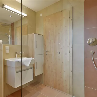 A modern bathroom with a shower, sink, and bright tiles. Towels are ready, and the decor is minimalist.