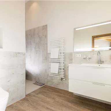 A modern bathroom with a bright, minimalist design. There is a shower, a sink, and a pleasant wood look on the floor.