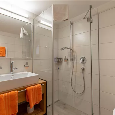 A modern bathroom with a shower and a sink. Orange towels add a colorful accent to the space.